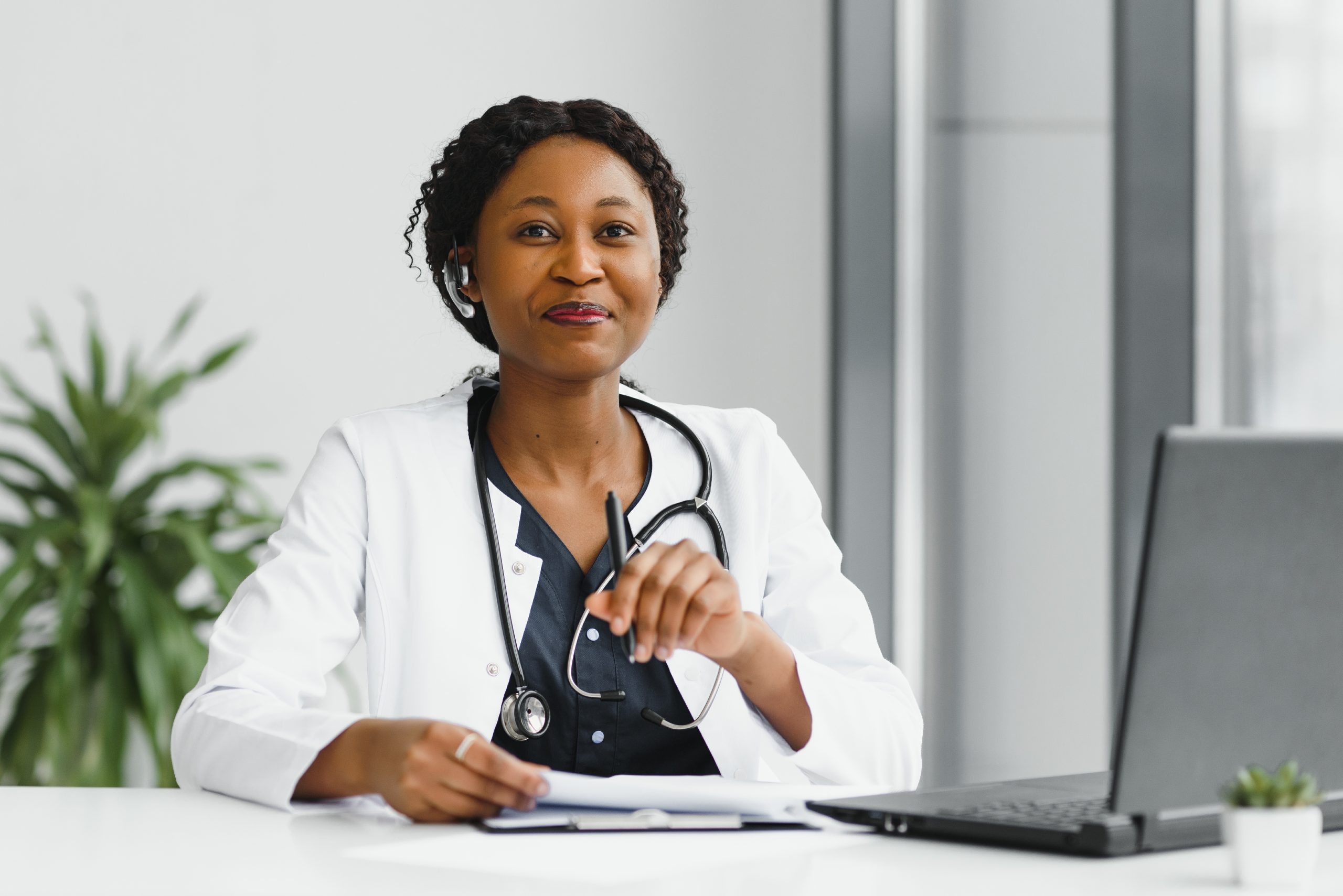 medicine, online service and healthcare concept – happy smiling african american female doctor or nurse with headset and laptop having conference or video call at hospital